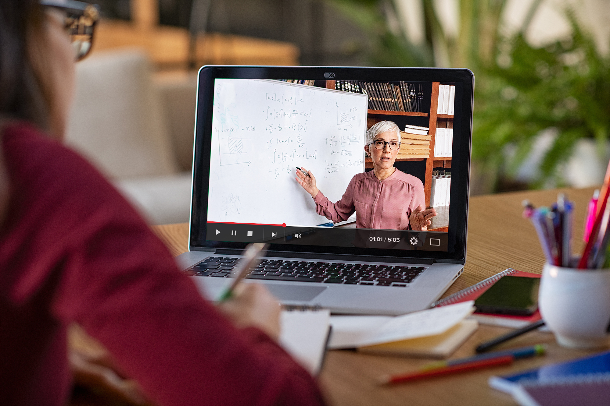 Studierende blickt auf einen Laptop, auf dem eine Lehrperson eine Rechnung an der Tafel zeigt.